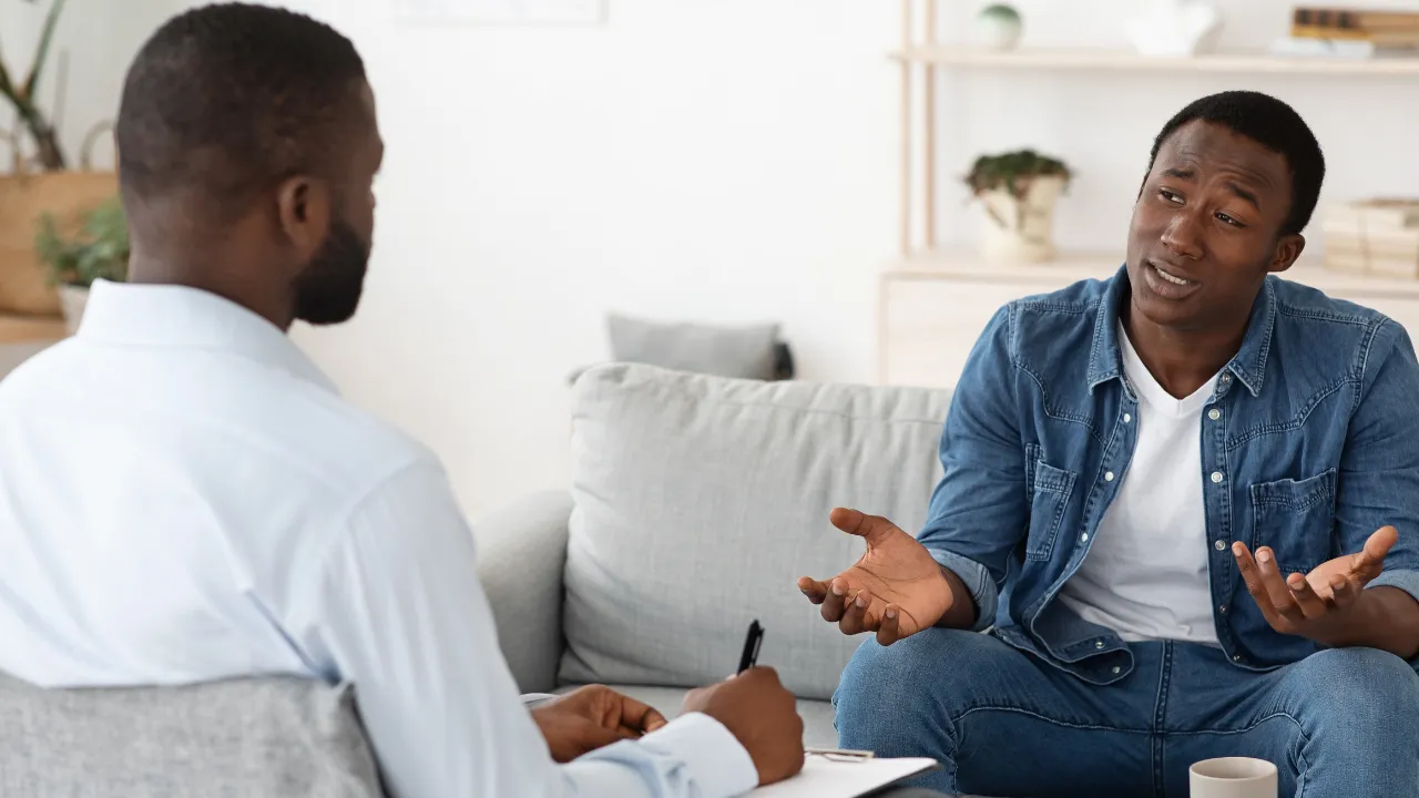 Two men are sitting on a couch talking.